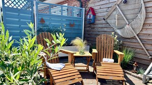 A patio with wooden chairs and a table, surrounded by plants and a blue gate. - Freie Sicht Das Nordsee-Gesundheitshaus 1 (Dagebuell)