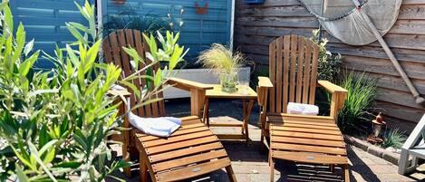 A patio with wooden chairs and a table, surrounded by plants and a blue gate.