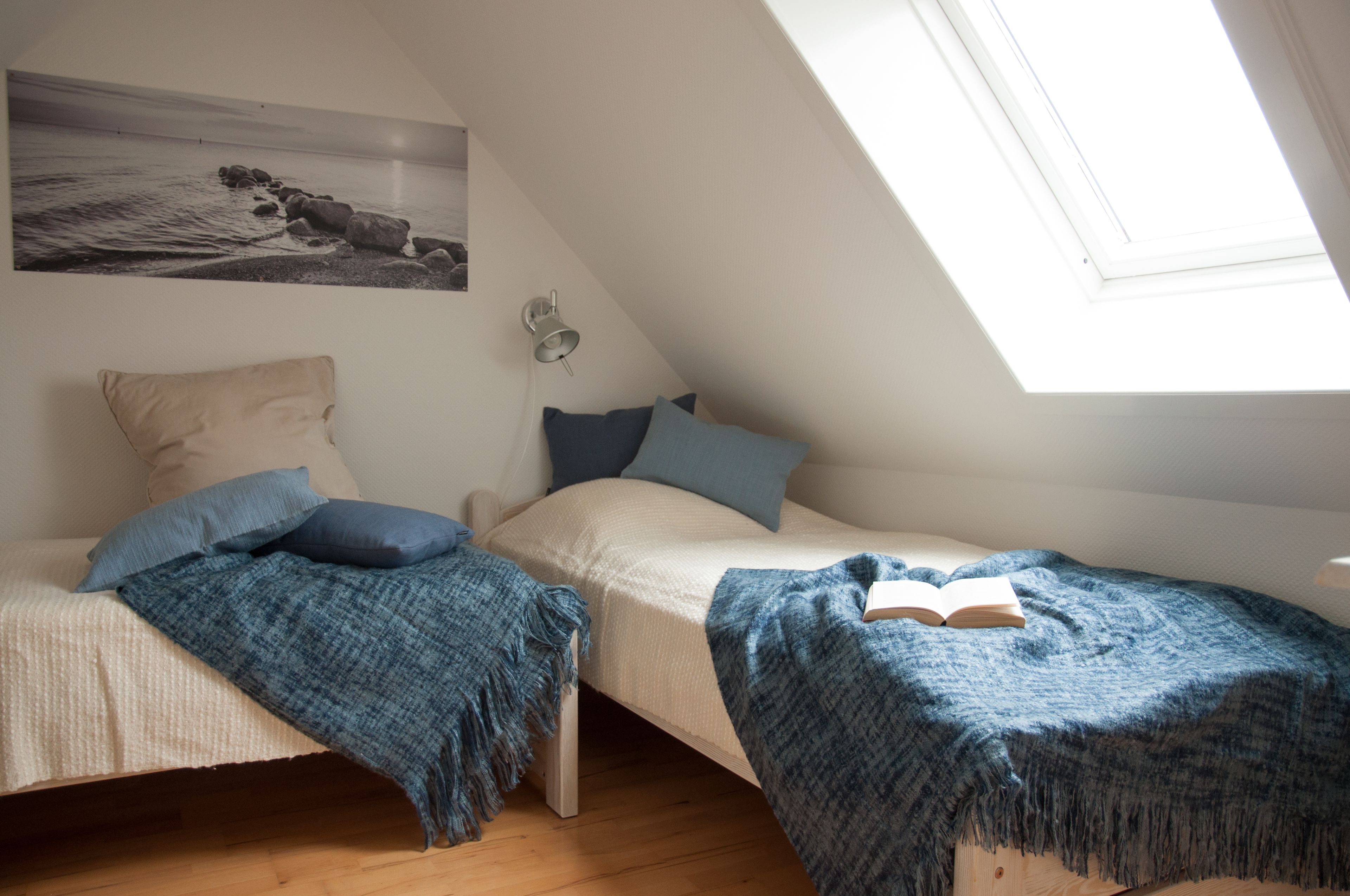 A bedroom with two beds, a skylight, a wall-mounted lamp, and a painting.