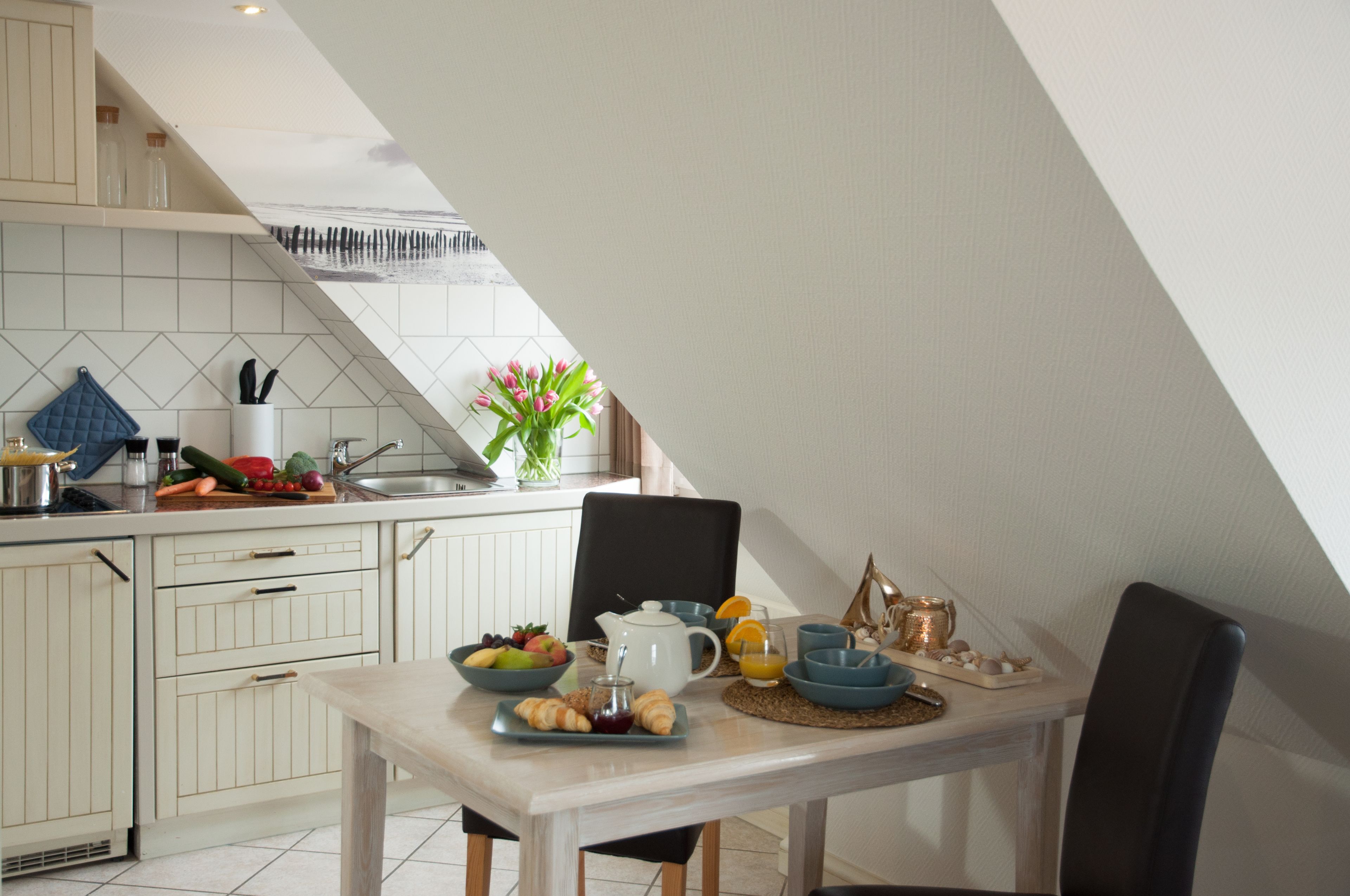 Une cuisine avec une table à manger mise pour le petit-déjeuner, comprenant des fruits, des croissants et une théière.