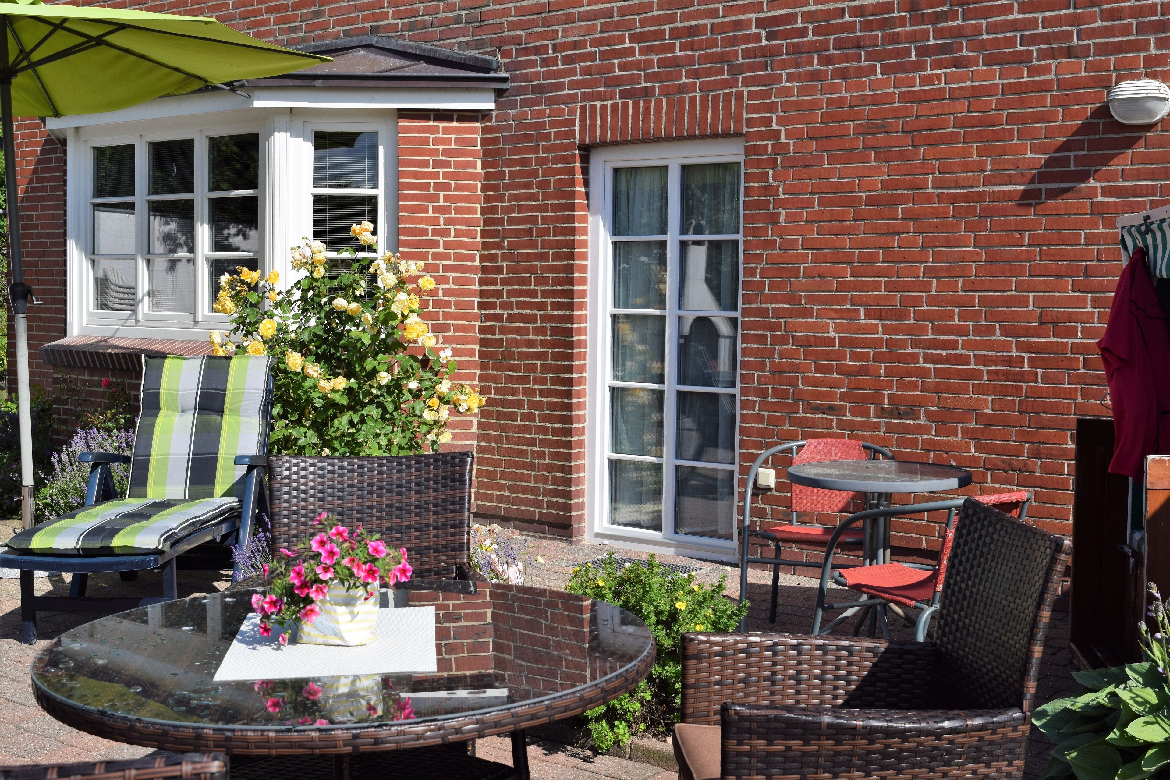 A patio with wicker chairs, a glass table, and a green umbrella.
