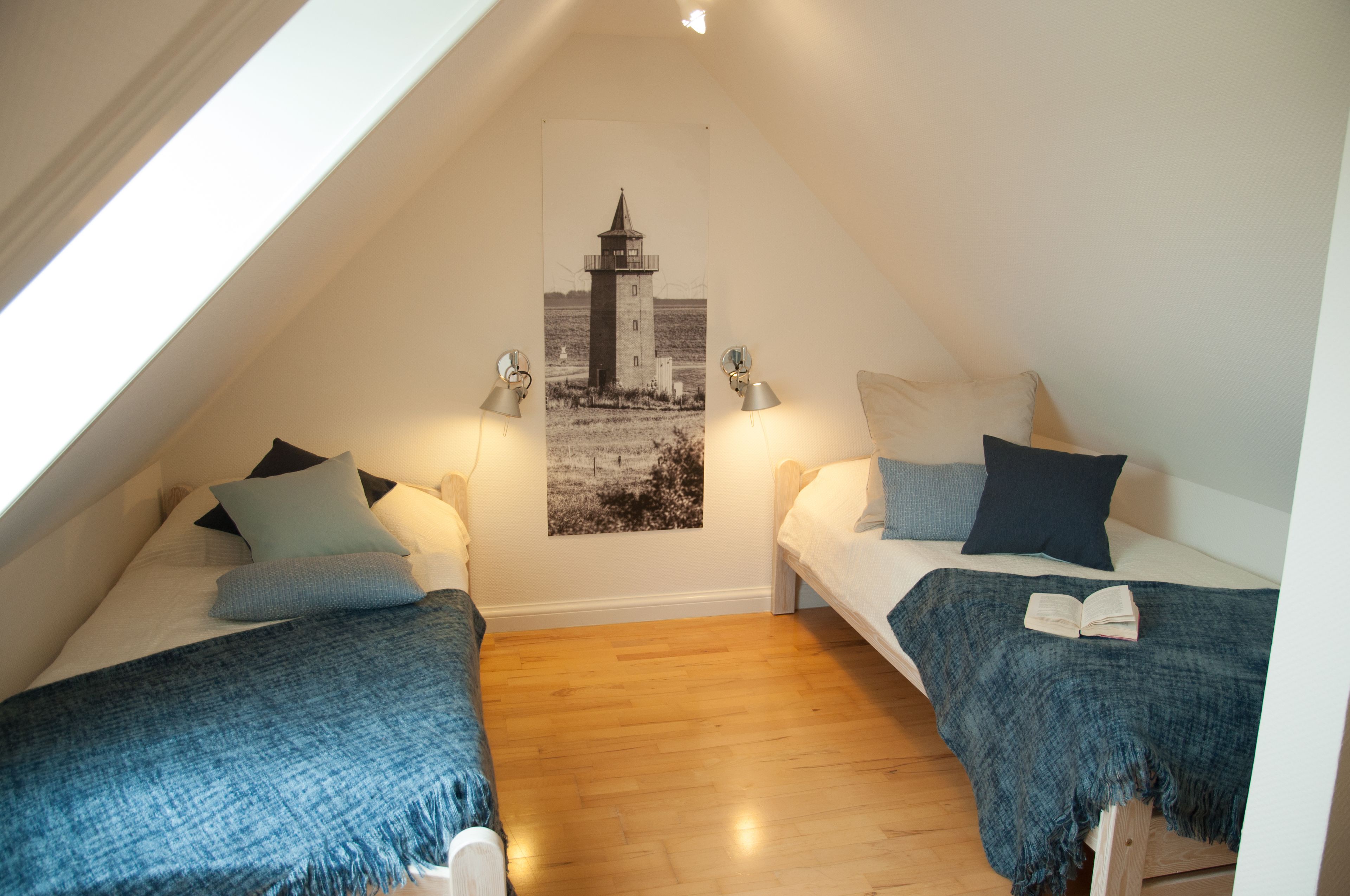 A cozy attic bedroom with two beds, a lighthouse poster on the wall, and a wooden floor.