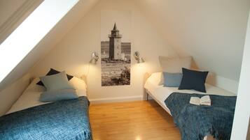 A cozy attic bedroom with two beds, a lighthouse poster on the wall, and a wooden floor.