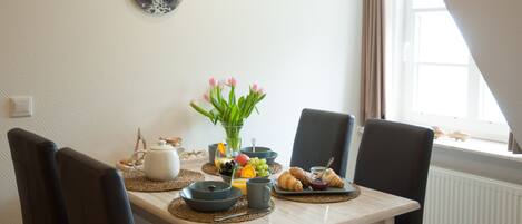 Een eettafel met ontbijtartikelen, een klok aan de muur en een raam met gordijnen.