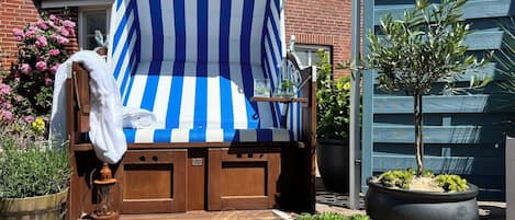 Ein Liegestuhl mit einem Streifenbaldachin, eine Holzbank und Kübelpflanzen.