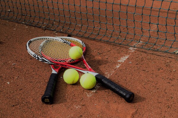 A tennis racket and two tennis balls on a clay court. - Freie Sicht Das Nordsee-Gesundheitshaus 1 (Dagebuell)