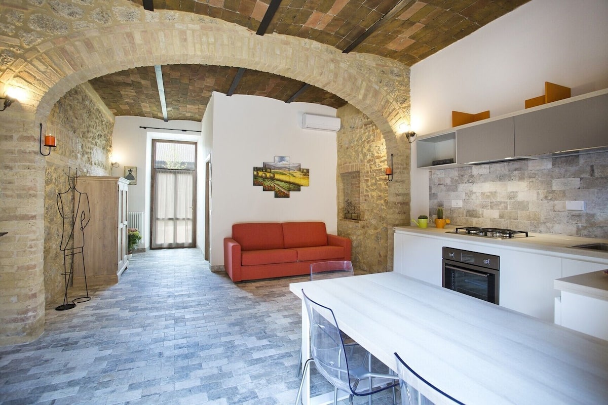 A modern kitchen with a stone archway, a red sofa, and a dining area with a white table.