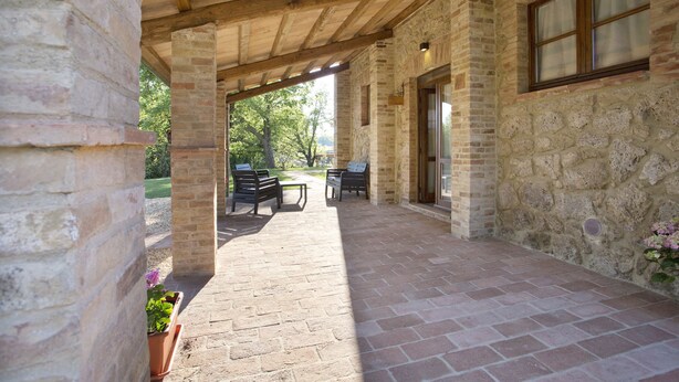A covered patio area with stone walls, wooden beams, and outdoor furniture.