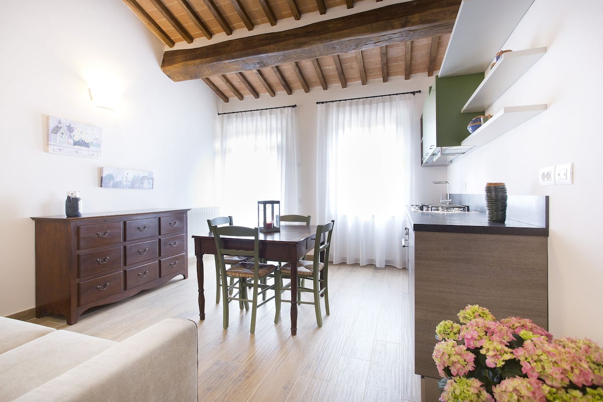 A dining area with a wooden table and chairs, a wooden cabinet, and a kitchen area with a countertop and cabinets.