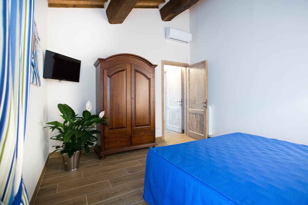 A bedroom with a bed, a wooden wardrobe, a potted plant, and a television on the wall.
