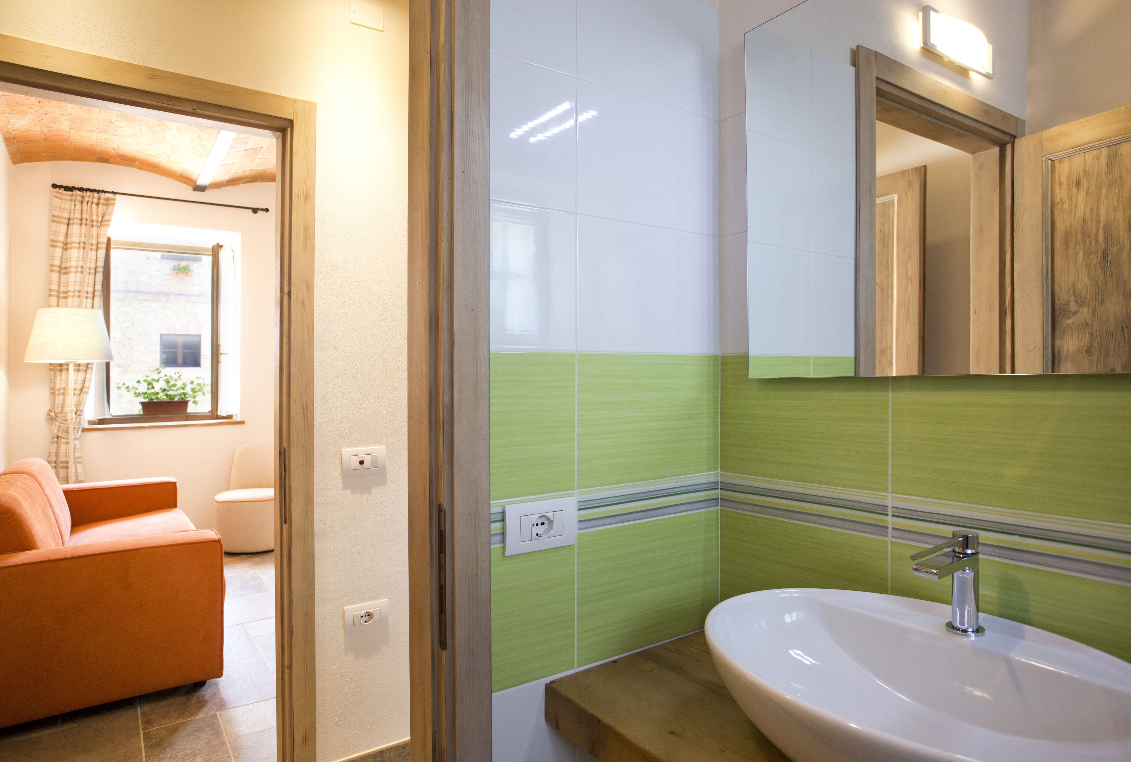 Un baño con un lavamanos blanco, baldosas verde rayadas y un tocador de madera.