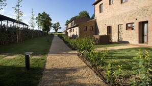 A pathway leading to a stone building with multiple windows and a covered area on the left.