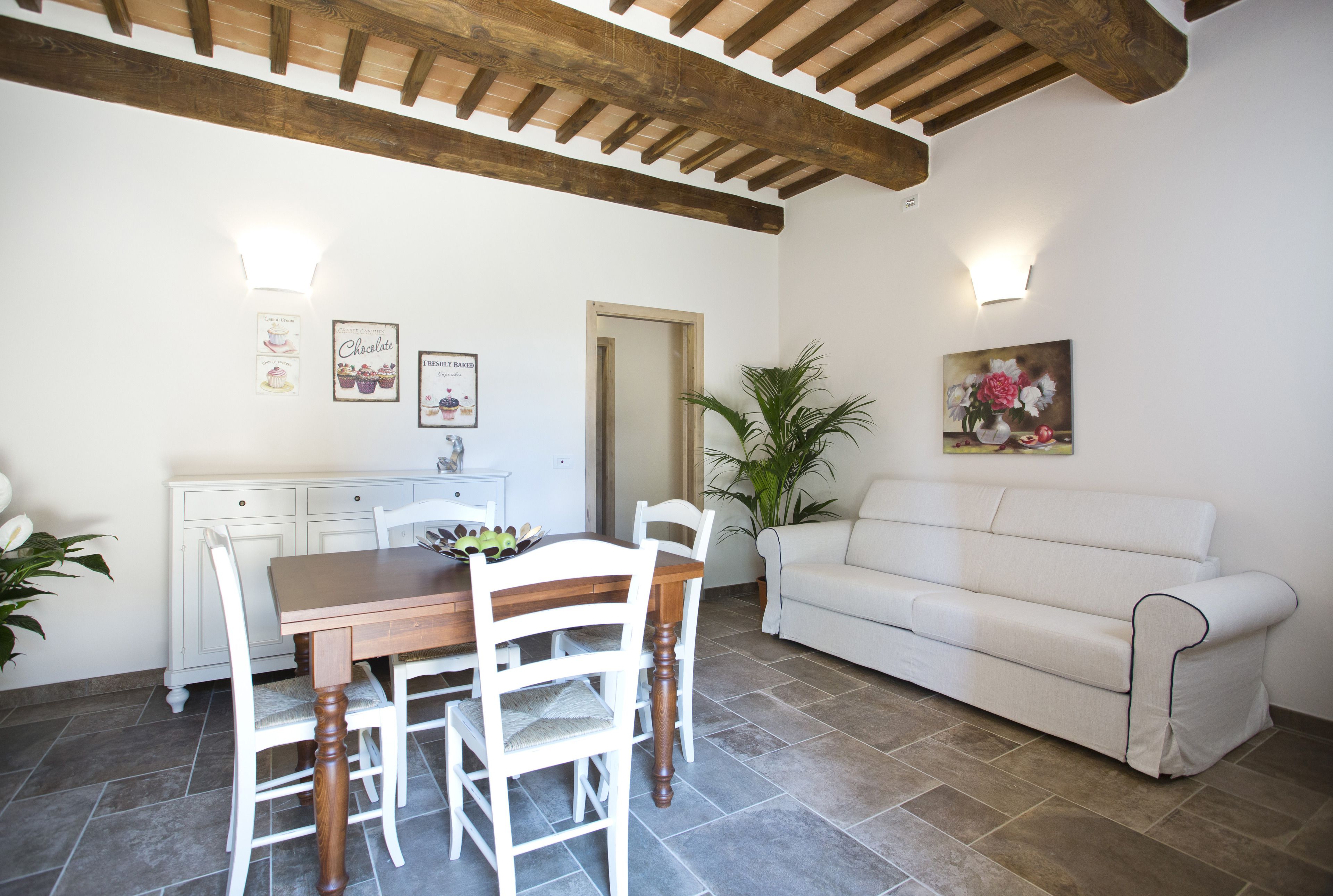 A dining area with a wooden table and white chairs, a white sofa, and a potted plant.