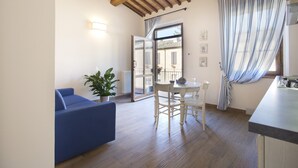 A room with a blue sofa, a dining table with chairs, a potted plant, and a view through a glass door to the outside.
