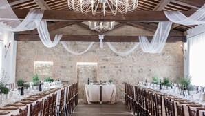 A long banquet table with chairs, a chandelier, and draped fabric on a stone wall.