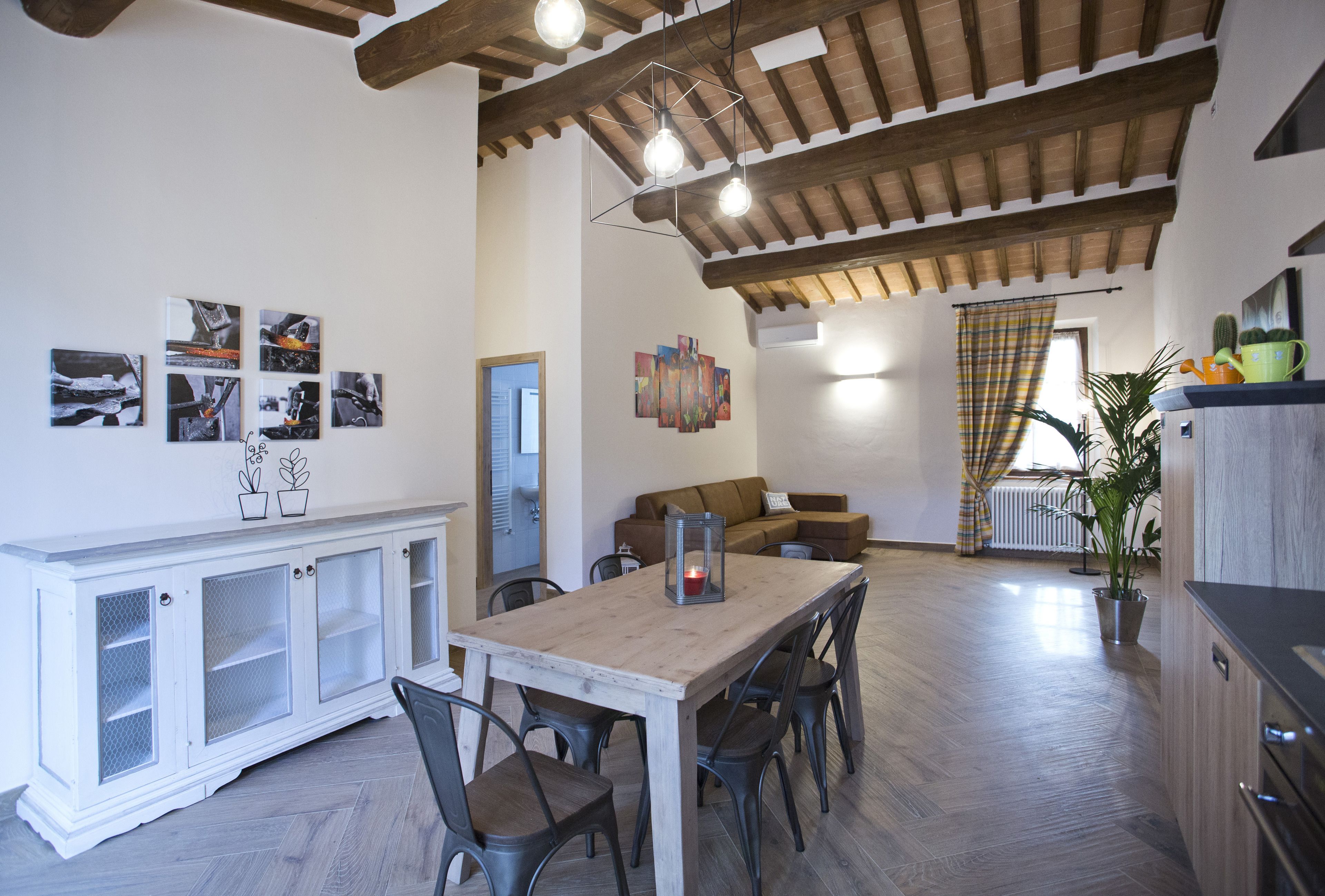 A spacious living area with a wooden dining table, chairs, a sofa, and a cabinet. There are wall art pieces and a potted plant.