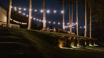 A nighttime outdoor gathering with string lights, a grassy hill, and trees.