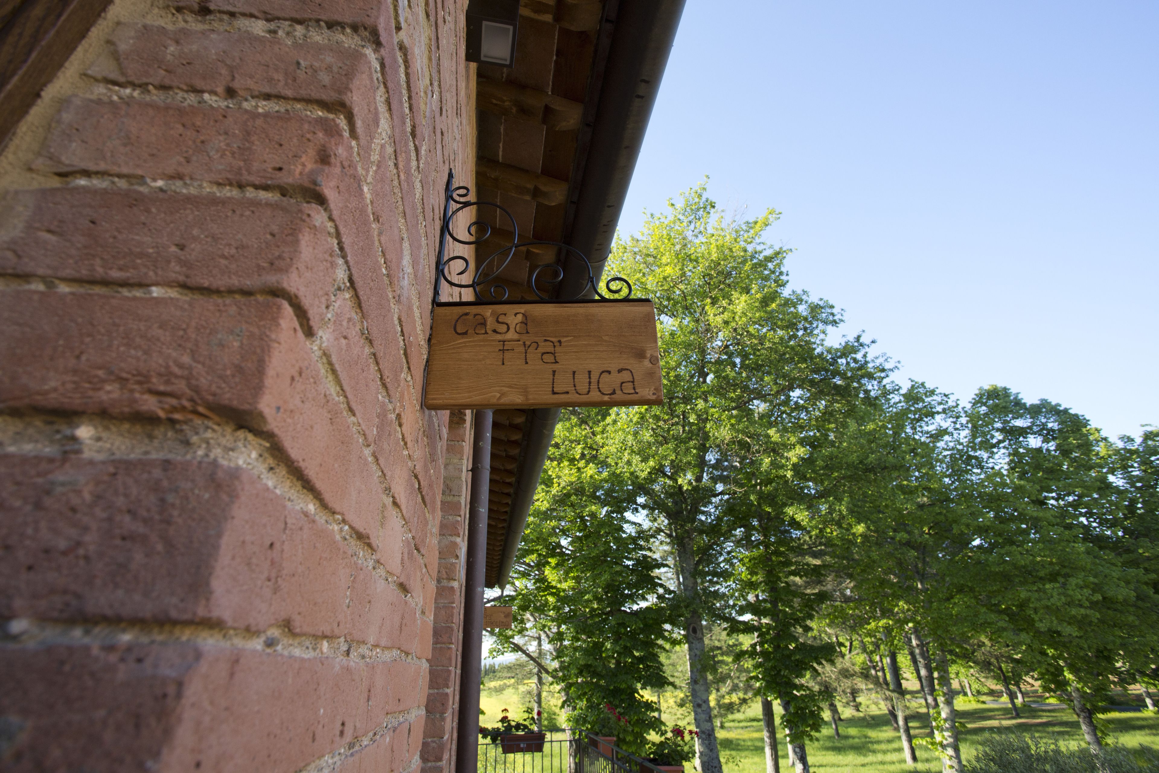 Un letrero de madera con el texto "casa Fra' Luca" sujeto a una pared de ladrillo.