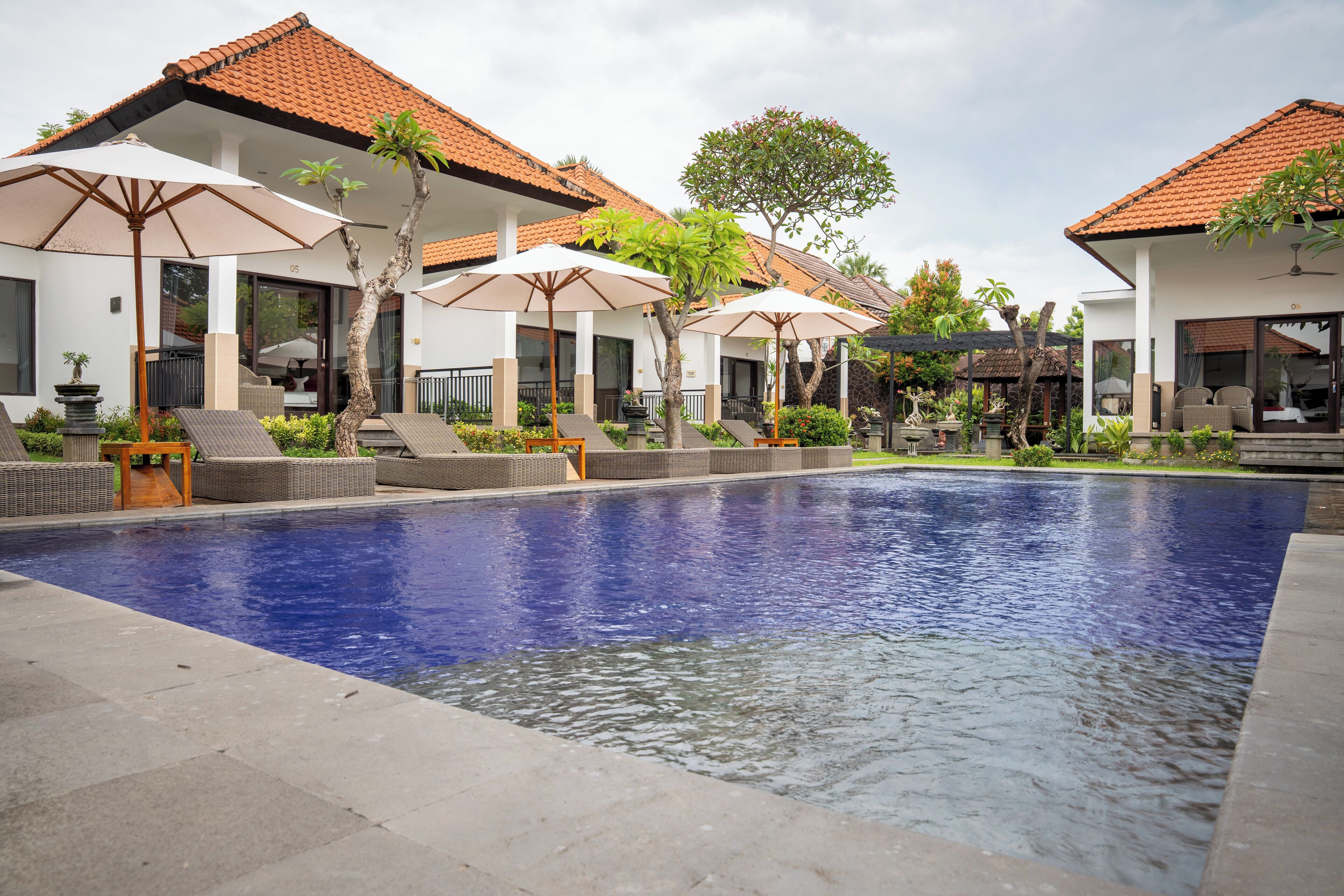 A swimming pool with lounge chairs and umbrellas, surrounded by buildings with tiled roofs.