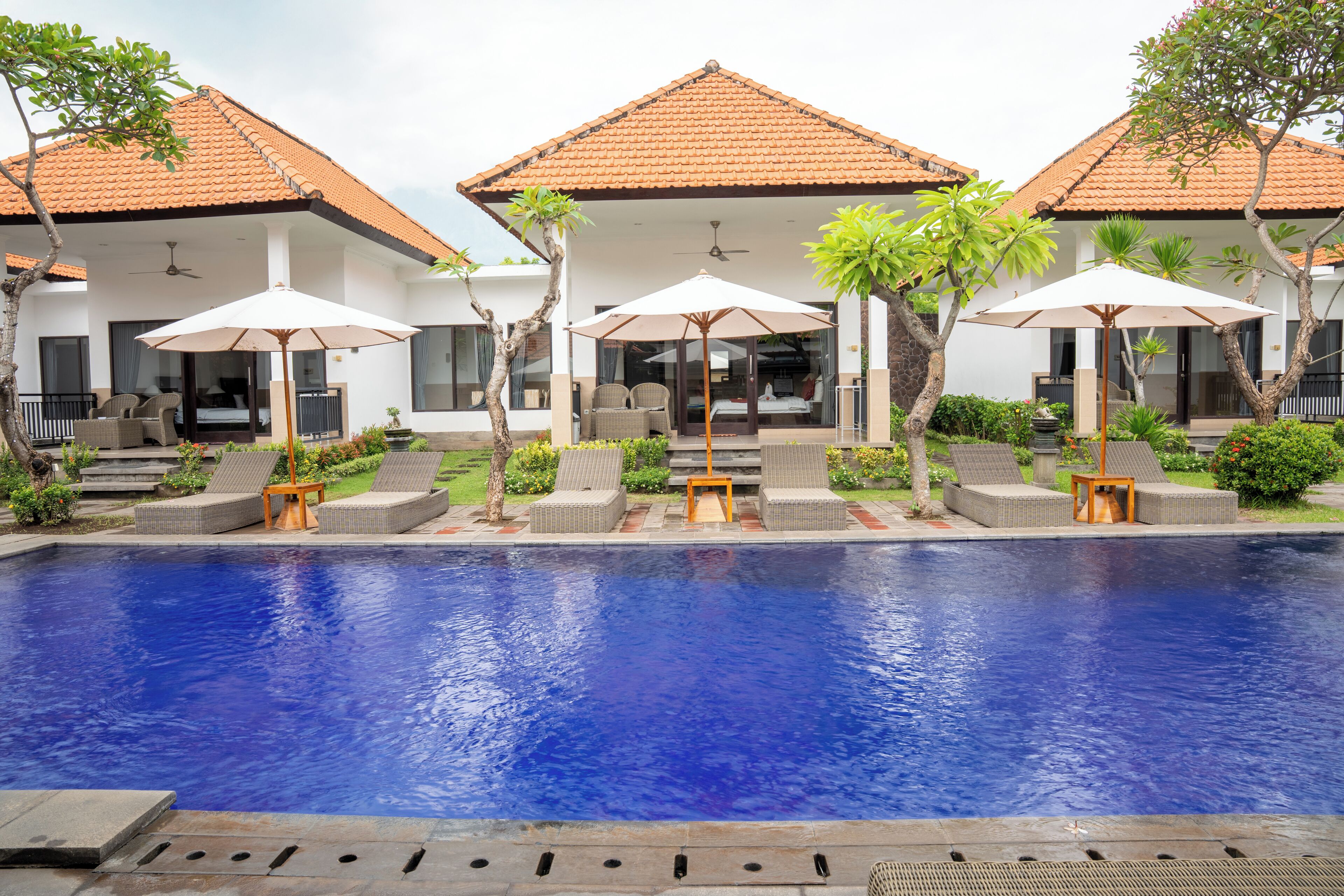 A poolside area with lounge chairs, umbrellas, and a clear blue pool.