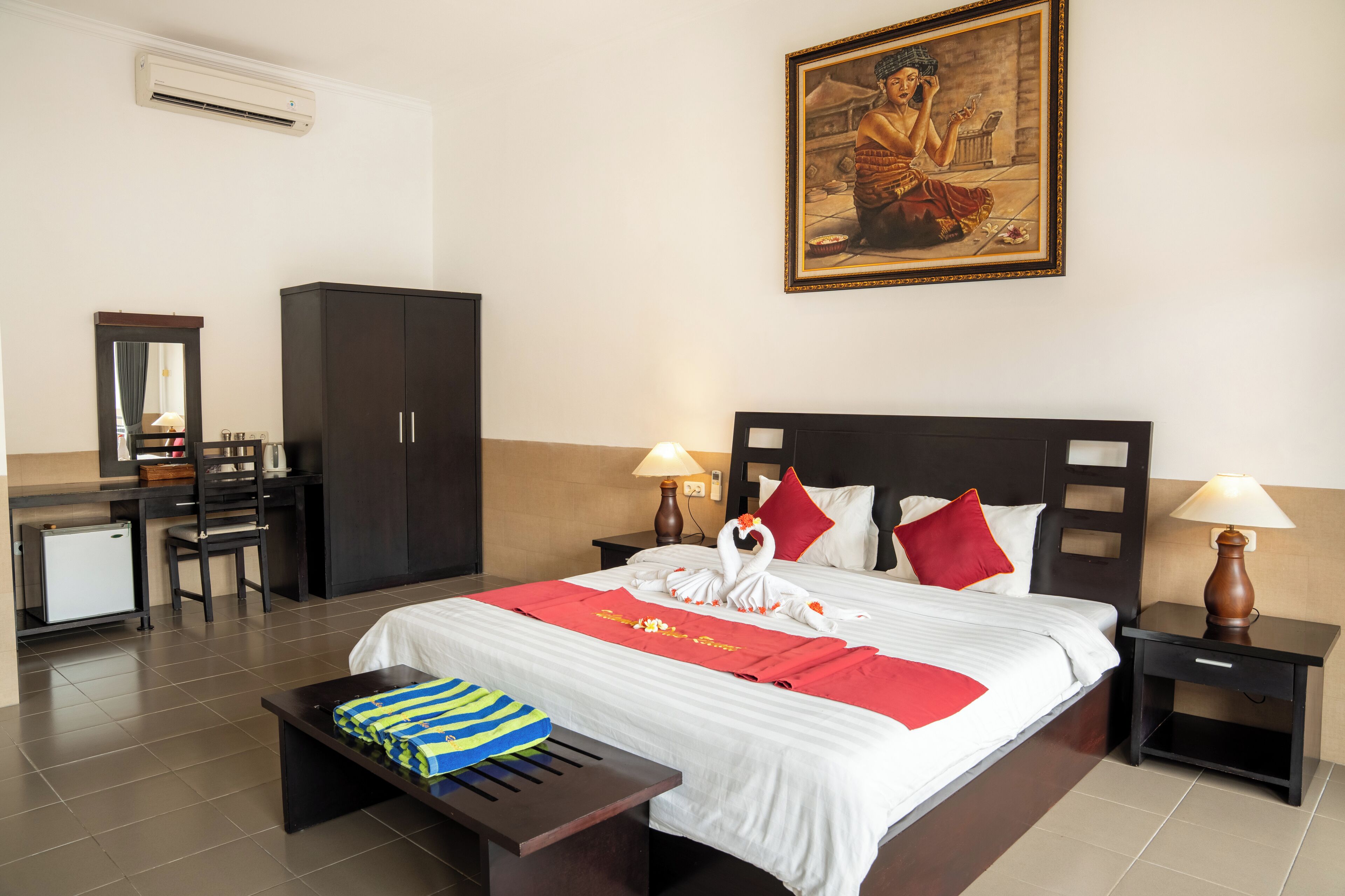 A hotel room with a bed, two bedside tables, a desk, a chair, a wardrobe, and a painting on the wall.