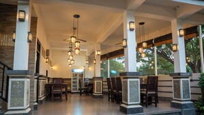 A covered outdoor seating area with chairs and tables, a refrigerator, and hanging lights.