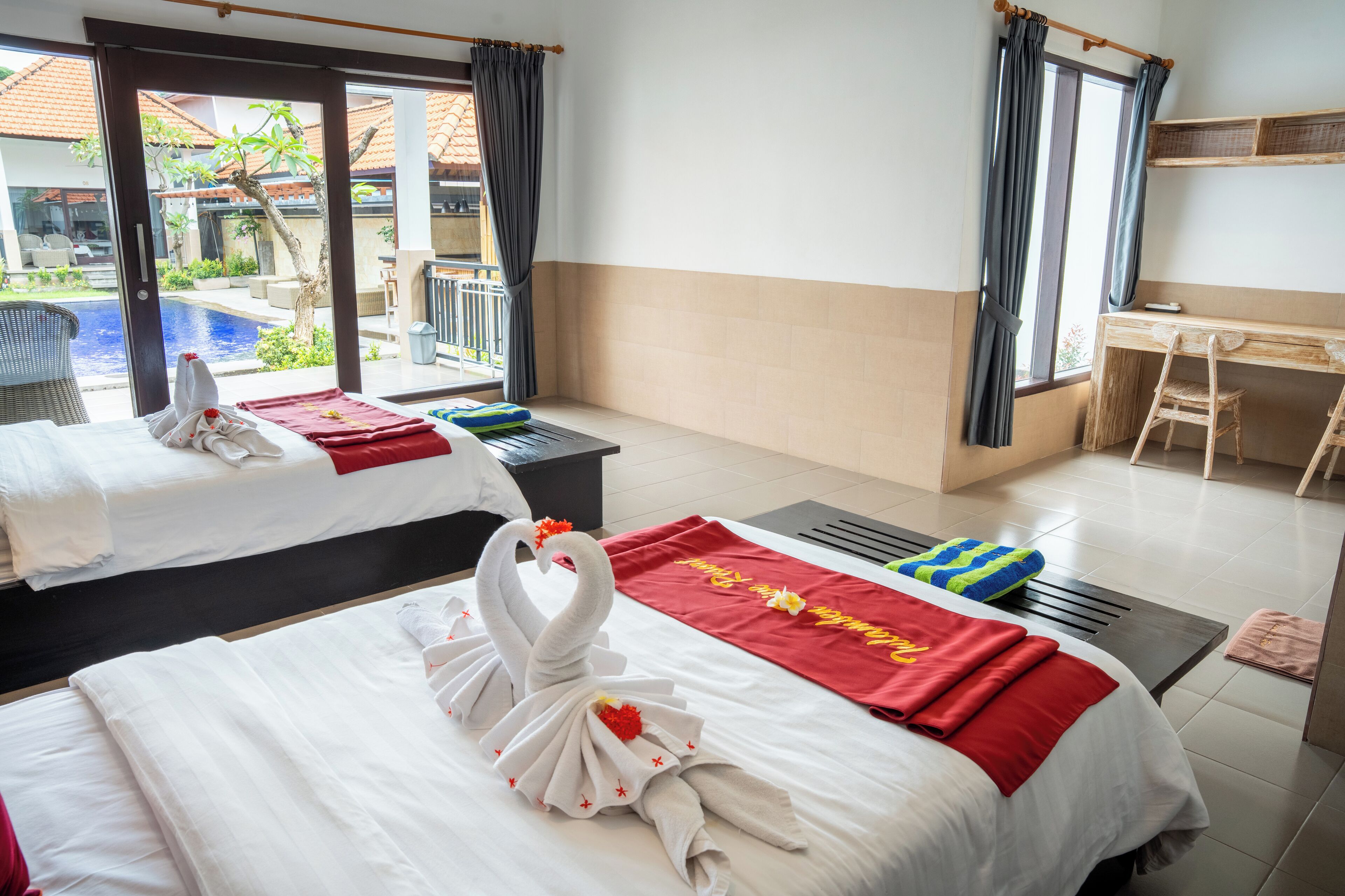 A hotel room with two beds, a desk, a chair, a view of a swimming pool, and a balcony.