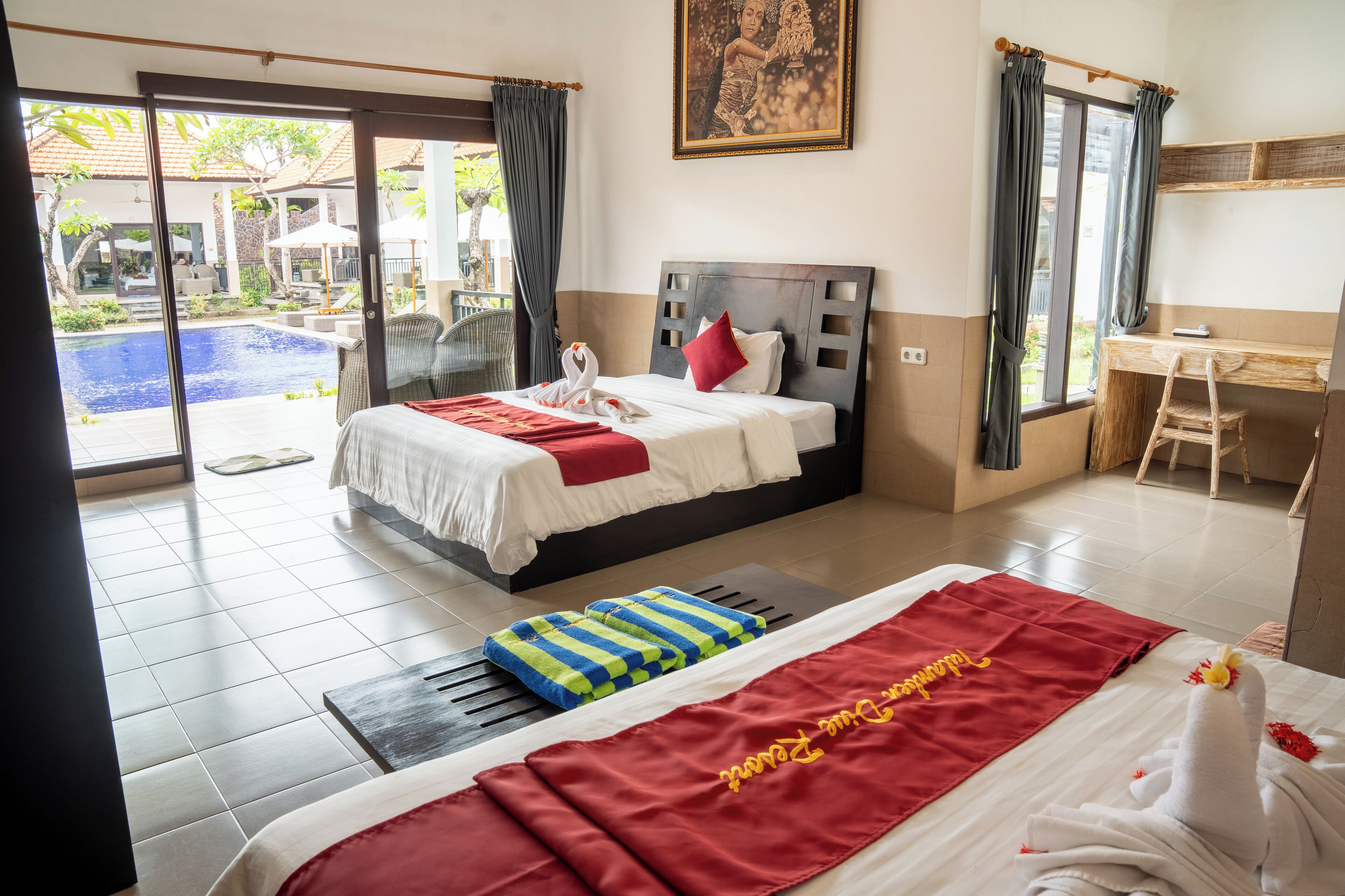 A hotel room with a bed, a desk, a chair, a massage table, and a view of an outdoor swimming pool.