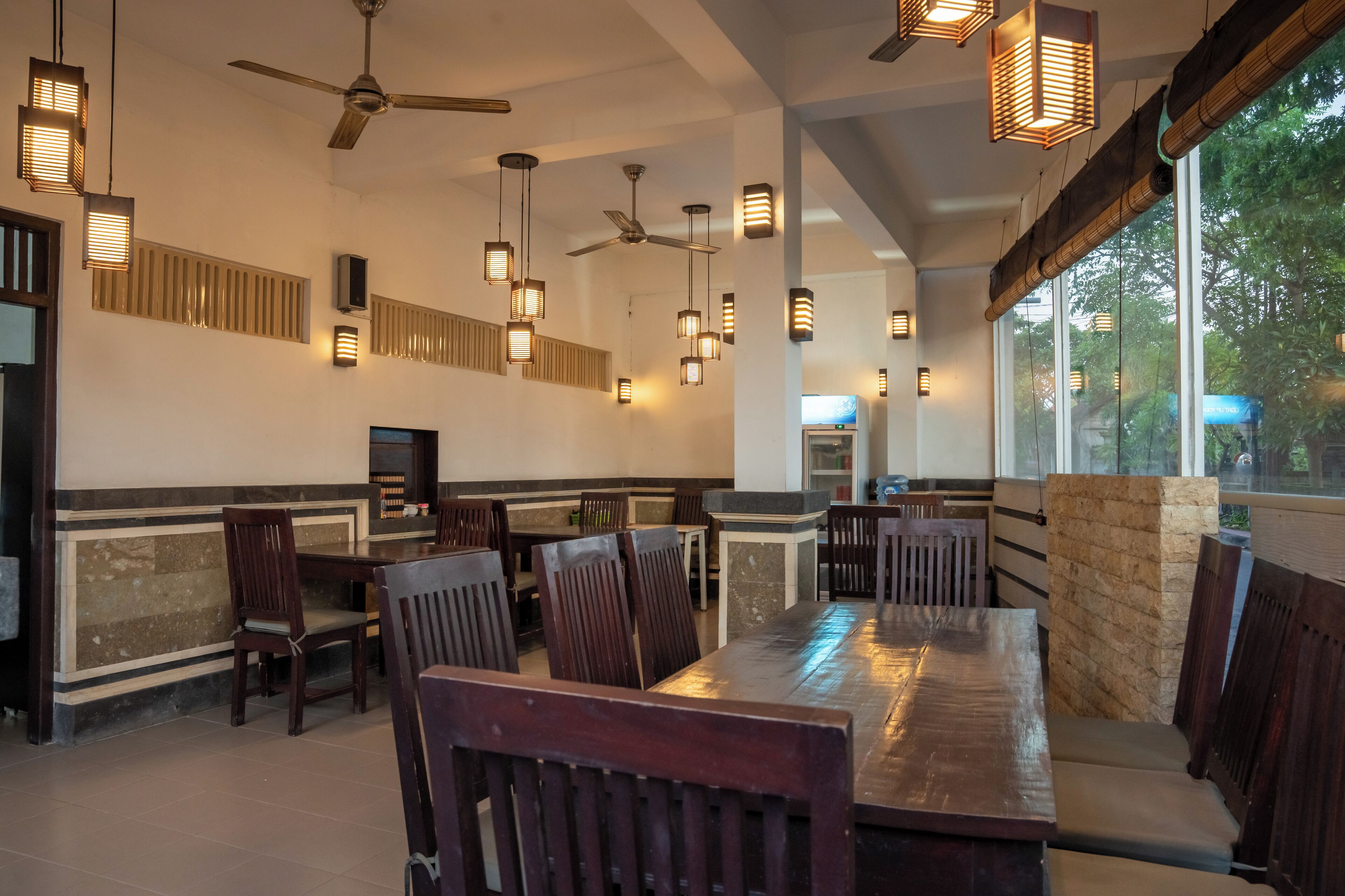 A restaurant with high ceilings, hanging pendant lights, and a large dining table with chairs.