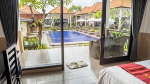 A hotel room with a view of a swimming pool, outdoor seating, and a balcony.