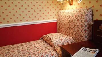 A small, cozy room with a single bed, a patterned headboard, and a table with a newspaper.