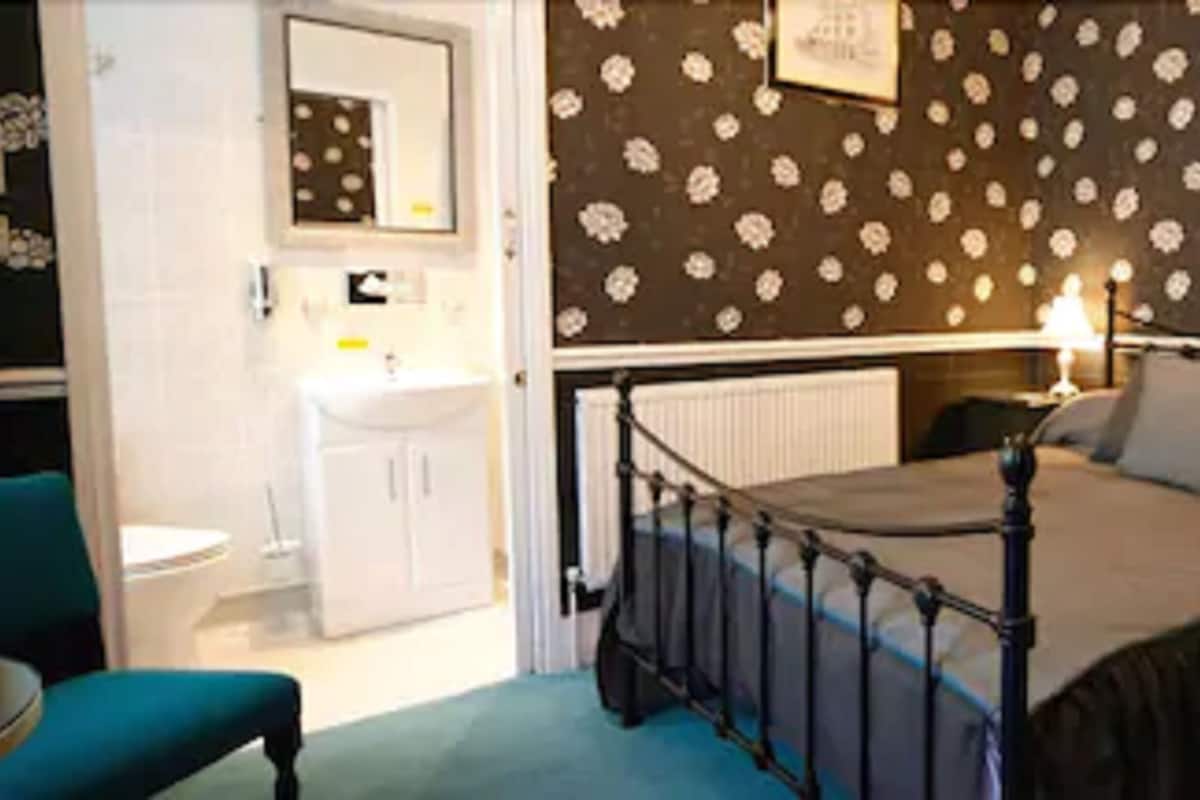 Een slaapkamer met een bed, nachtkastjes, een stoel, en een badkamer met een wastafel en spiegel.