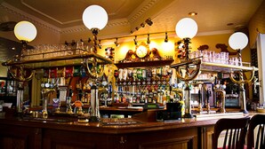 Een bar met een houten toonbank, verschillende biertaps en een ruim assortiment flessen en glazen.