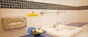 Une salle de bain avec un panneau d’avertissement indiquant que l’eau est très chaude, un porte-serviettes et un lavabo avec un récipient en verre.