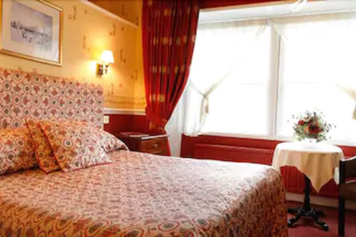 Een hotelkamer met een bed, een stoel, een tafeltje en een raam met gordijnen.
