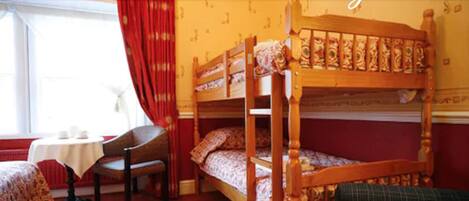 A room with a bunk bed, a table with chairs, and a window with red curtains.
