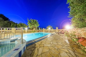 A swimming pool with stone flooring and a metal railing, surrounded by a fence and trees. - Parys Villas (Zakynthos)