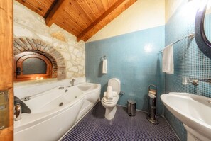 A bathroom with a stone arch, a bathtub, a toilet, and a sink. - Parys Villas (Zakynthos)