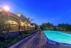 A wooden deck leading to a swimming pool with a stone building in the background. - Parys Villas (Zakynthos)