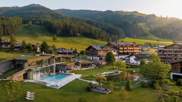 Et resort med swimmingpool, moderne og traditionelle bygninger samt bjerglandskab i baggrunden.