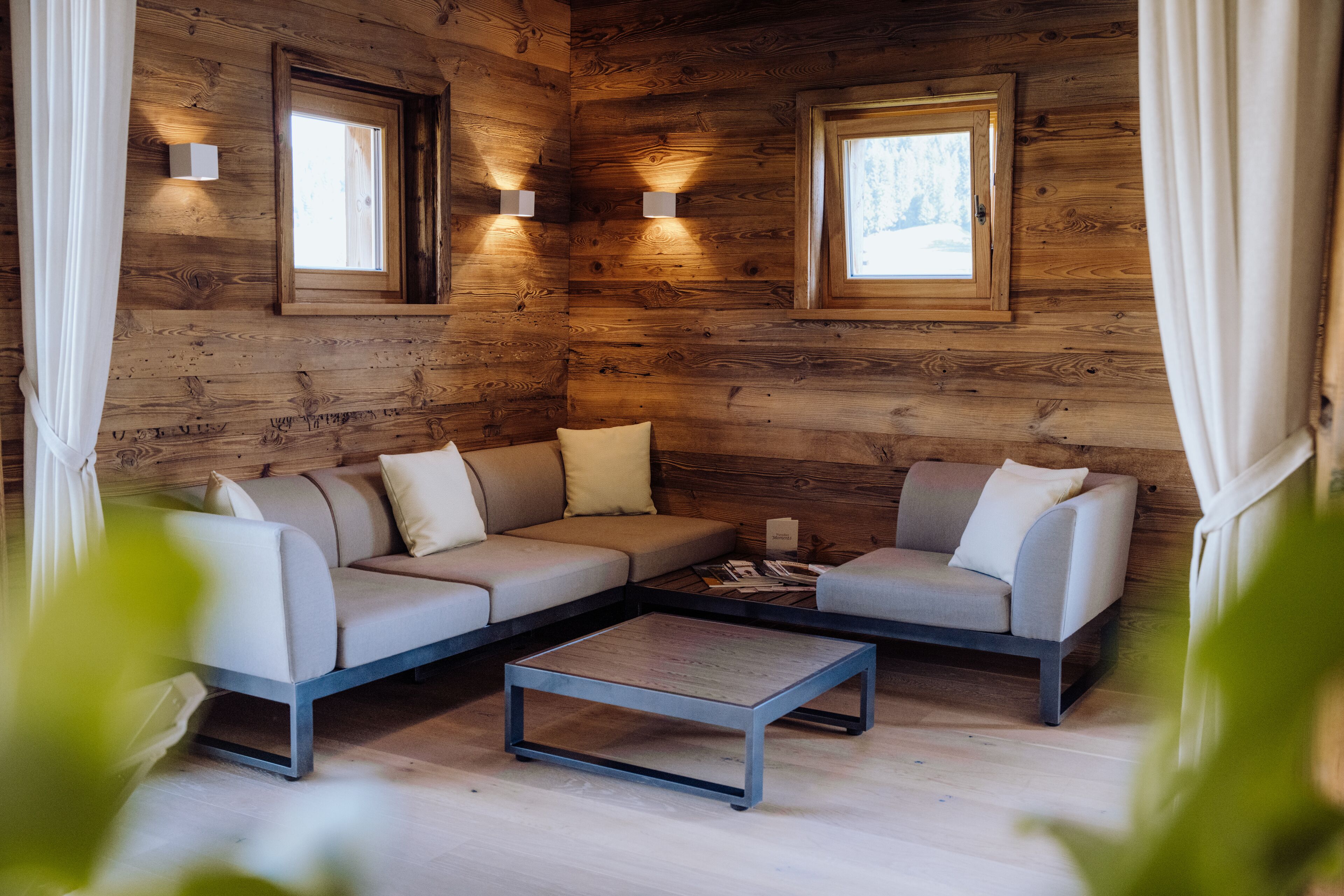 Interior acogedor de una cabaña de madera con un sofá modular, una mesa de centro y dos lámparas de pared.