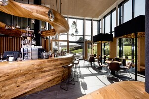 Et moderne barområde med trædiske, barstole og store vinduer med udsigt over det fri.
