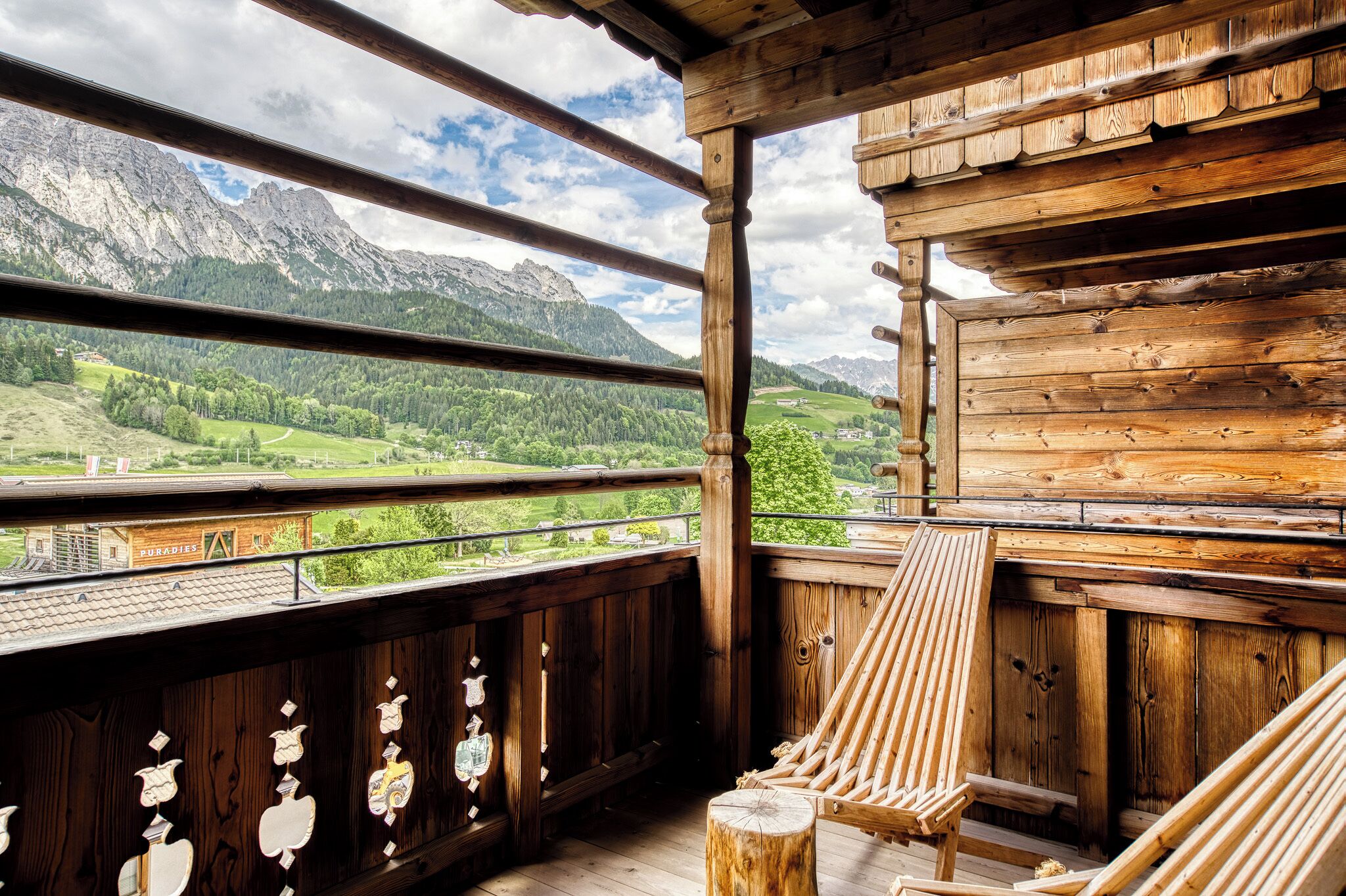 A wooden balcony with a view of mountains and a green valley.