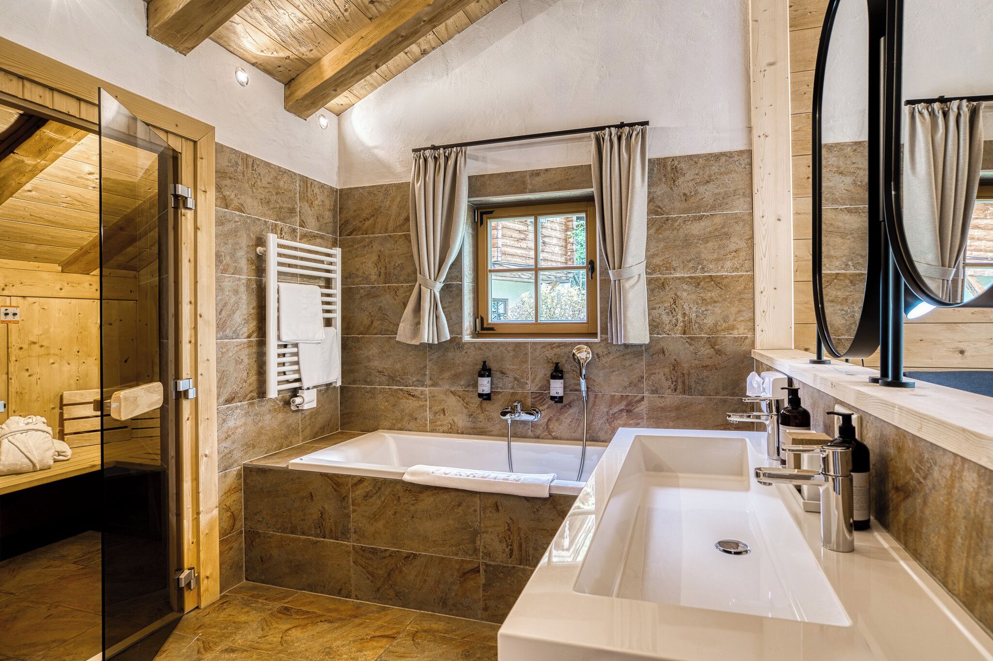 A modern bathroom with a bathtub, a large sink, a glass shower enclosure, and a window with curtains.