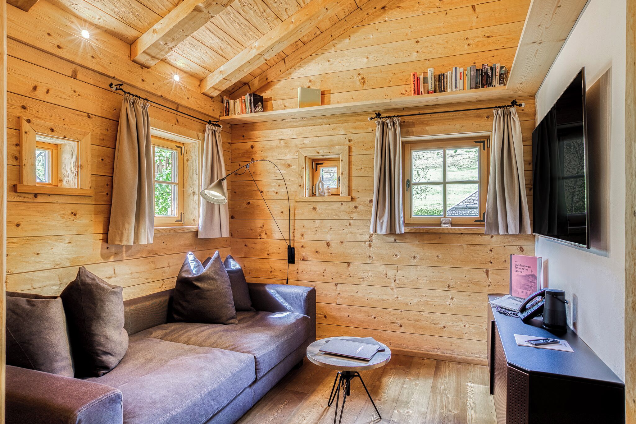 Interior de una cabaña de madera con un sofá, una mesita, un escritorio con teléfono y un televisor.
