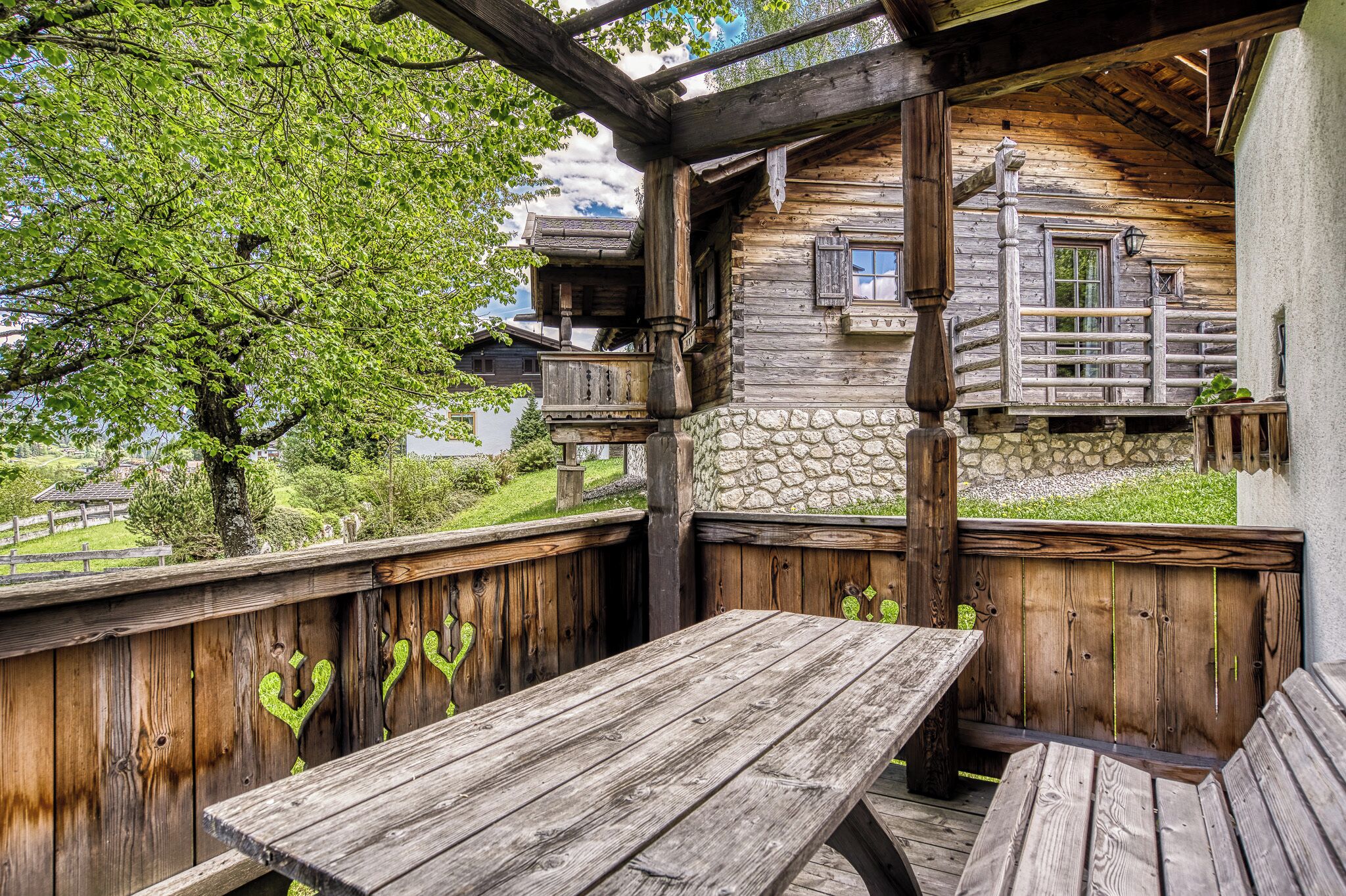 A wooden deck with a table and benches, a stone wall, and a wooden building with a balcony.