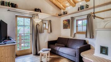 Una habitación acogedora con suelo de madera, un sofá, una mesita, un televisor y una chimenea.