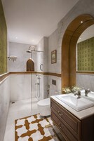 A modern bathroom with a marble shower, a toilet, a sink with a mirror, and a patterned rug.