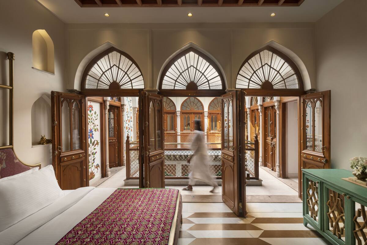 Una habitación de hotel con una cama grande, una consola verde y vistas a un patio a través de puertas arqueadas.