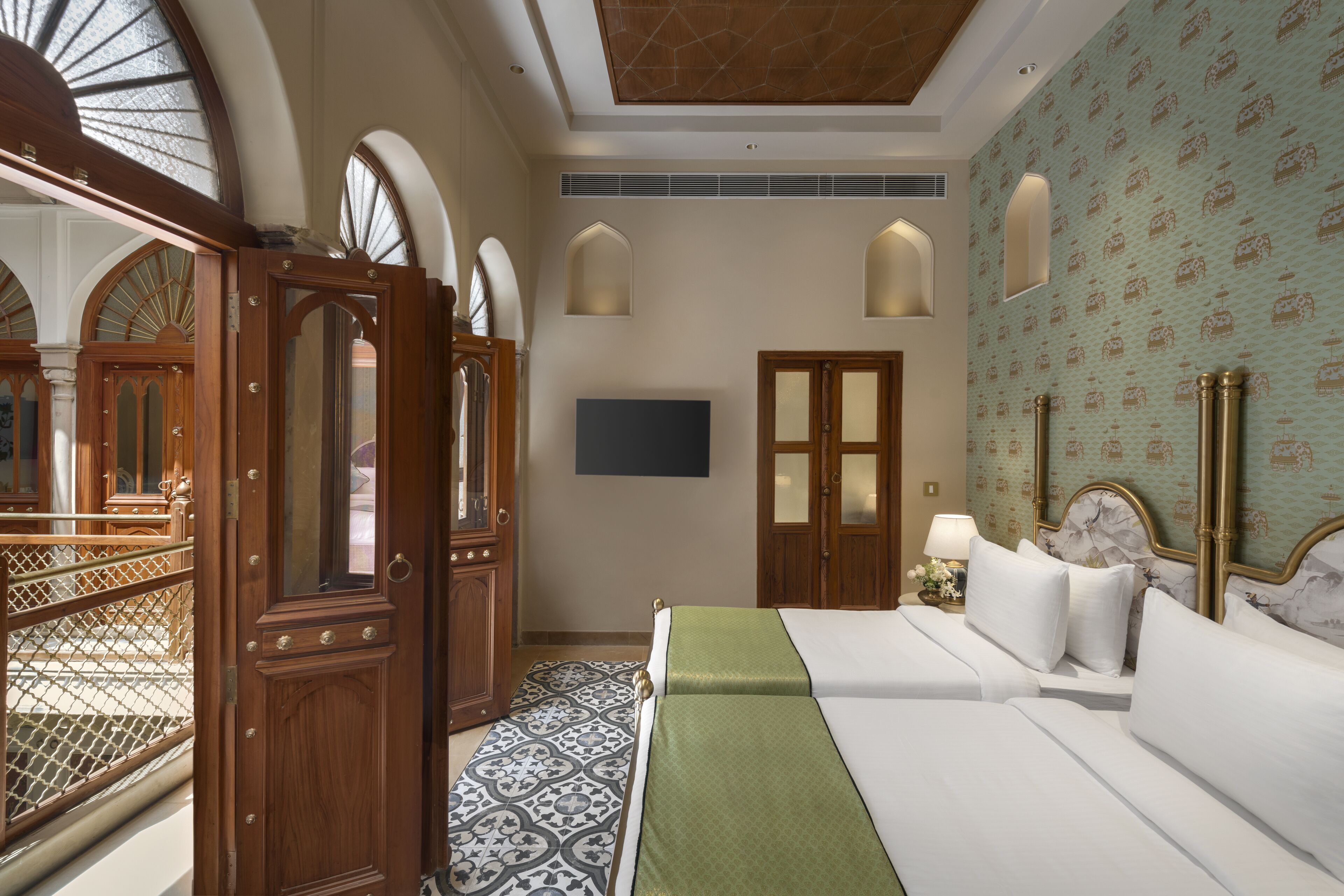 Quarto de hotel com uma cama grande, um espaço de estar com uma poltrona, uma porta de madeira e parede com padrão.